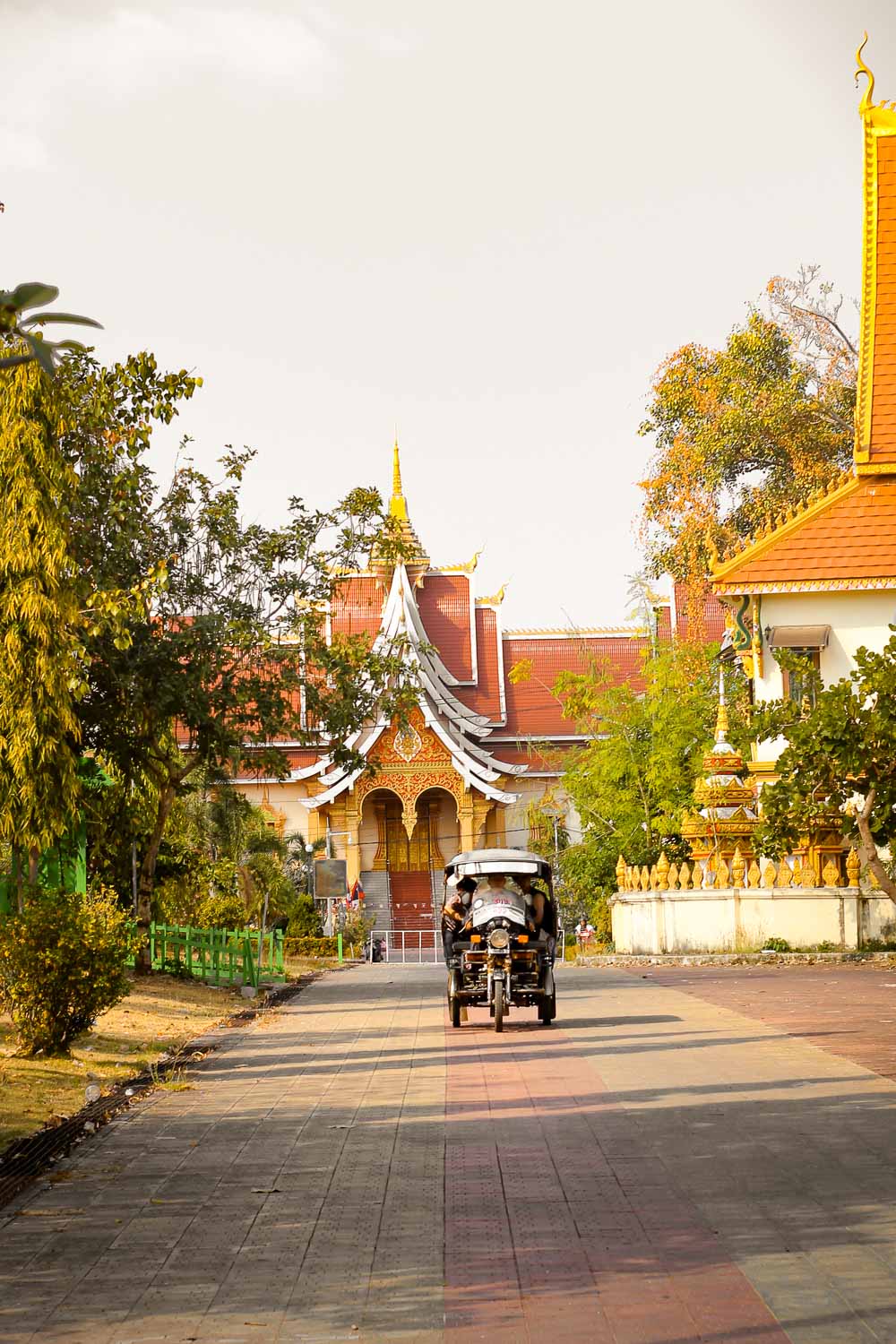 A tuk Tuk approaching in Vientiane with a fantastic Buddhist temple in the foreground